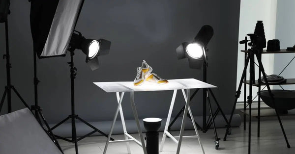 In a photography studio, a pair of sneakers sits on a table. The table is lit by three-point lighting.