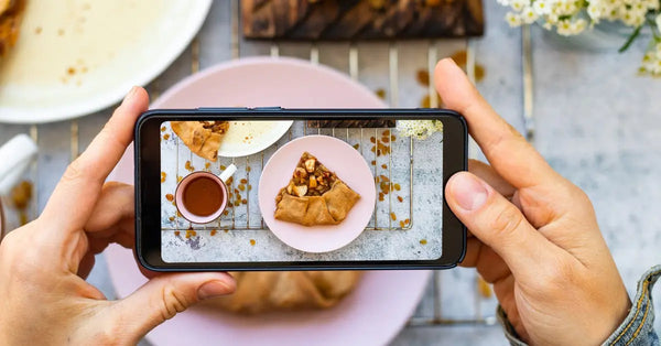 A person’s hands hold a smartphone and point it downward towards a plate of delicious homemade apple pie.