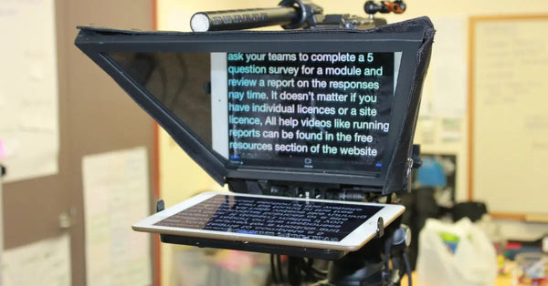 A teleprompter mounted on a tripod and set up inside a room. The script on the screen is in large white font.