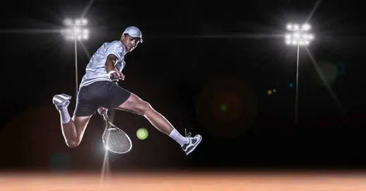 A tennis player in black shorts leaps dynamically through the air, reaching to hit the ball with his paddle.