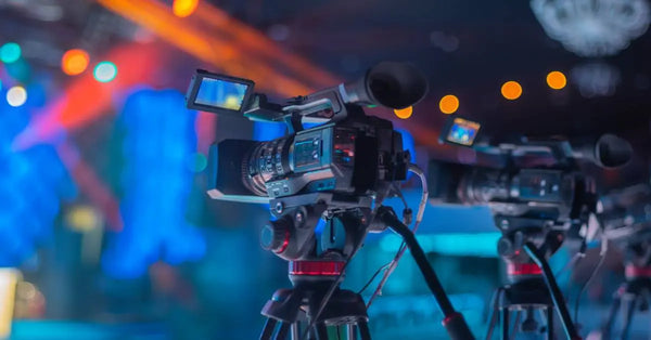 Three cameras on tripods are lined up in front of a concert hall, lit brightly in shades of blue with no people around.