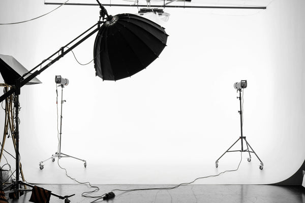 An empty photography studio, outfitted with several studio lights. A large, plain white backdrop is hung up.